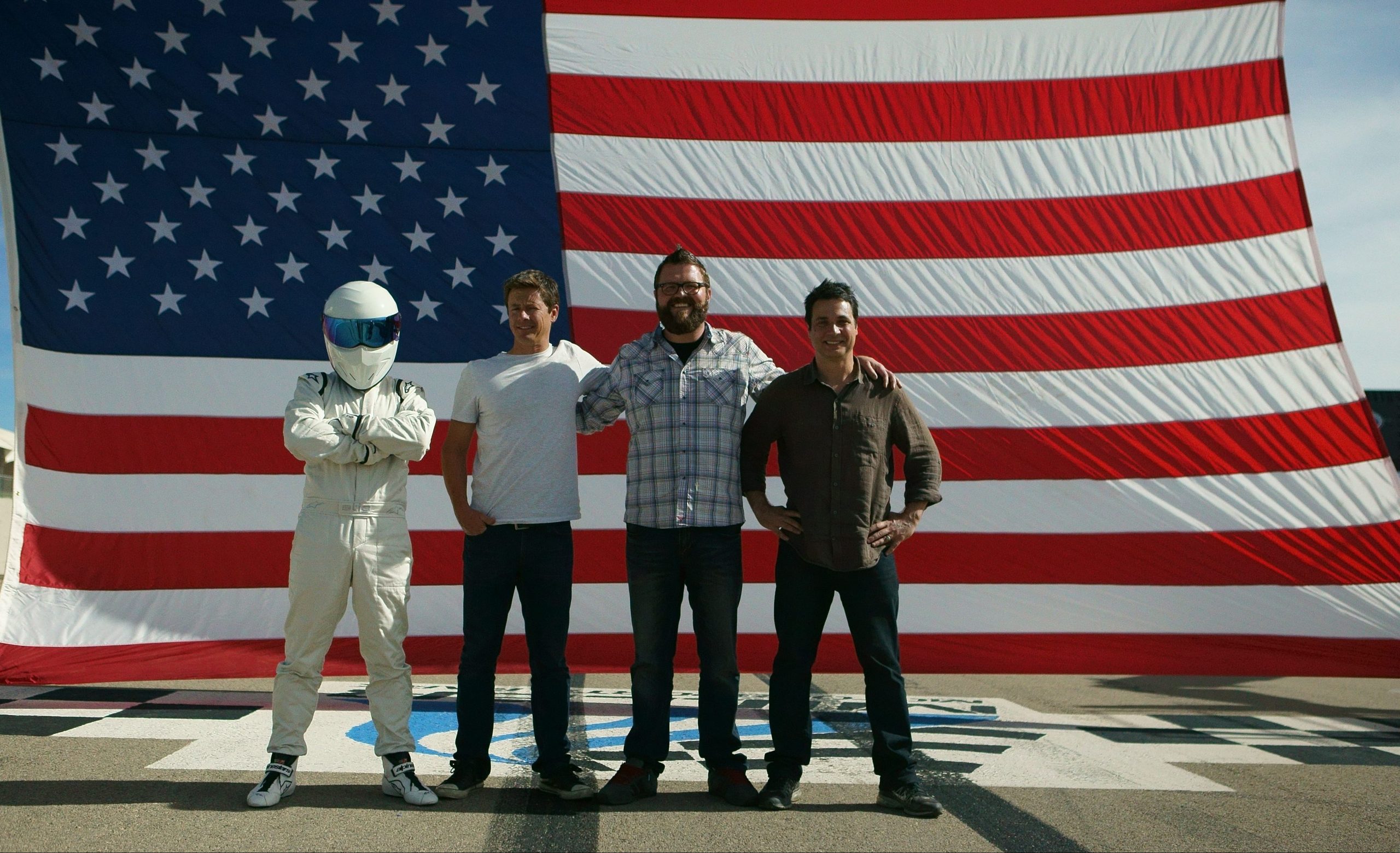 Picture Shows: Tanner Foust, Rutledge Wood, and Adam Ferrara with Stig in front of American Flag