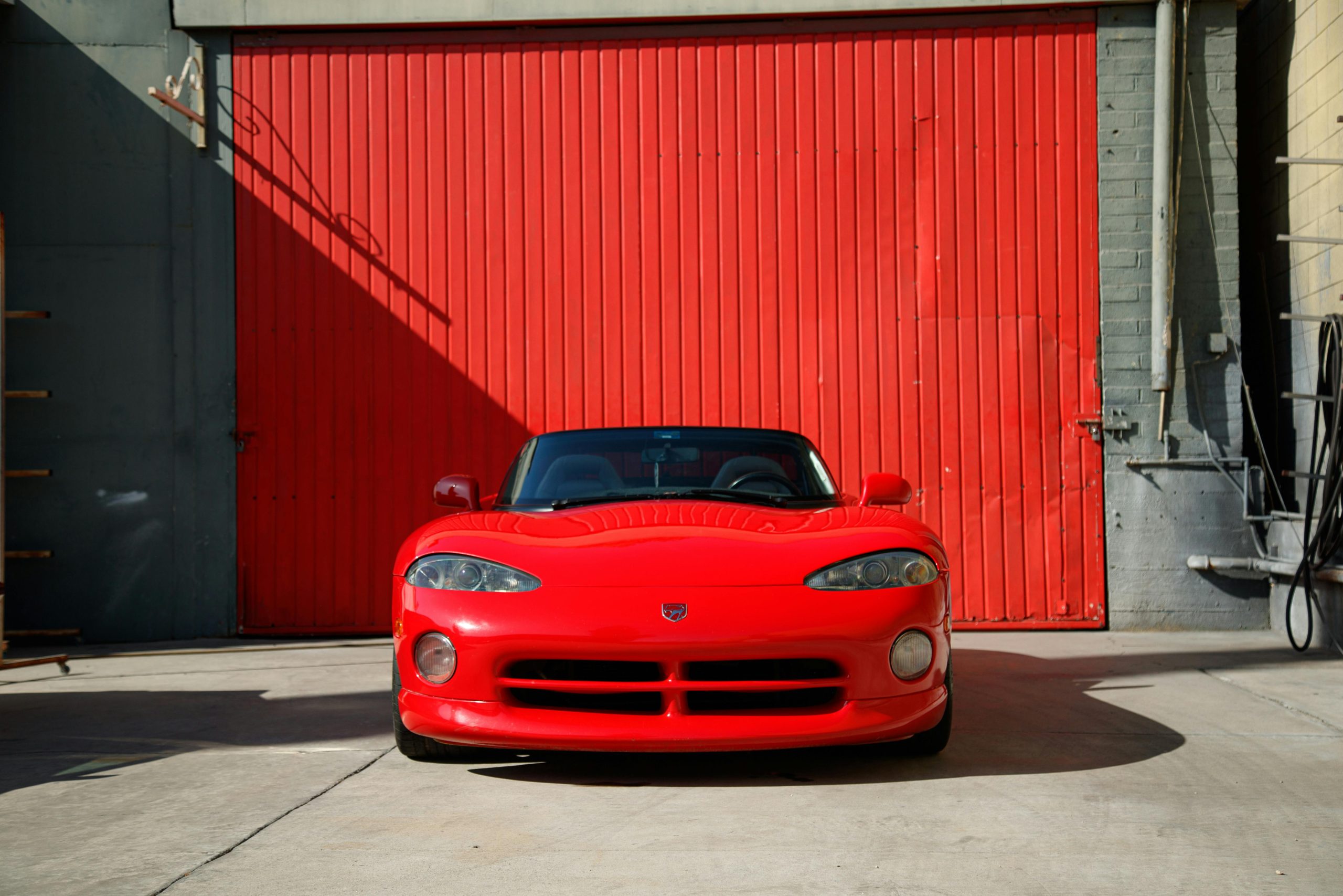 Bold red Dodge Viper sports car parked in front of an industrial red wall, showcasing sleek design.